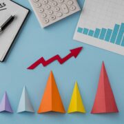 Top-down view of business growth items featuring a red rising arrow, a success notebook, a calculator, and colorful 3D cones on a blue background